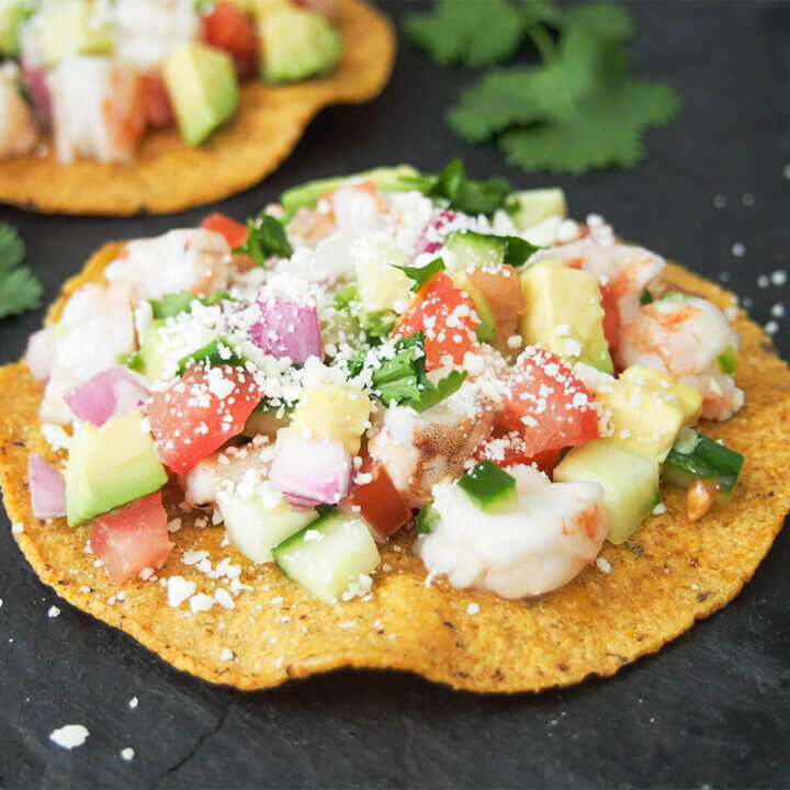 shrimp ceviche tostada with part view of another behind and cilantro on board