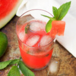 glass of watermelon mojito showing ice in top of glass and mint and melon garnish
