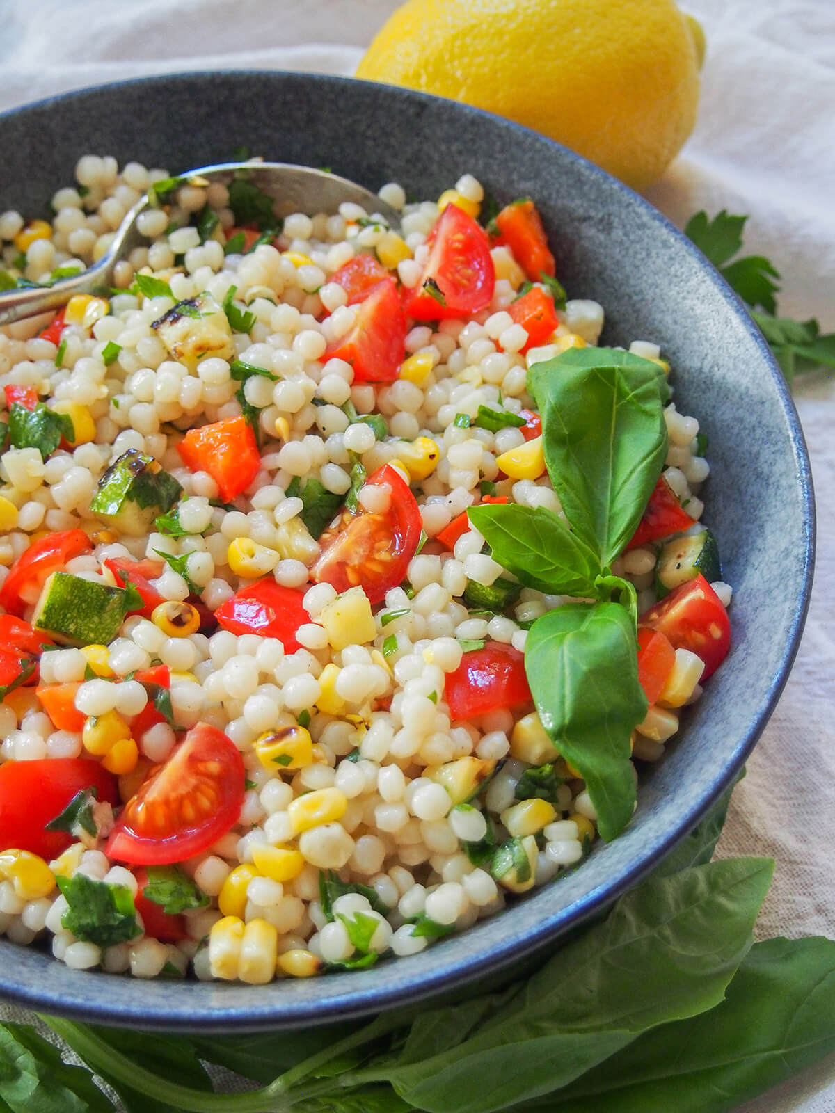 side view of bowl of Israeli couscous salad with grilled vegetables garnished with basil