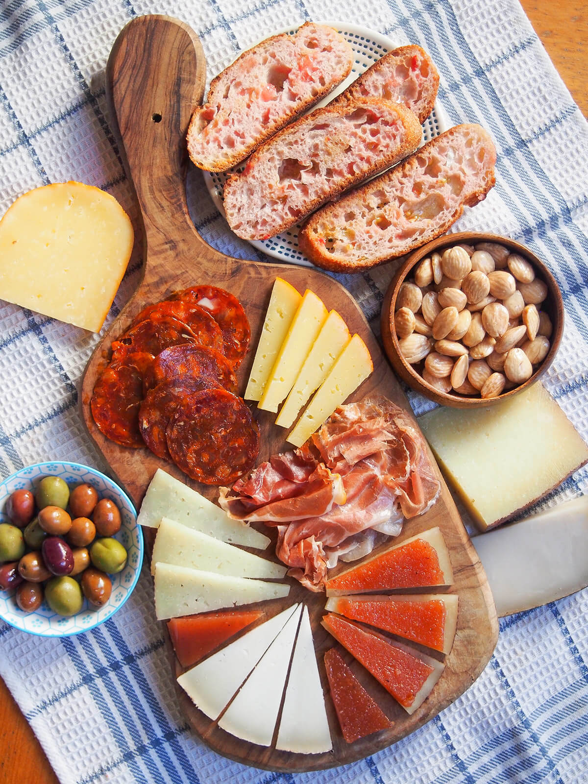Spanish cheese board with plate of tomato bread above and pieces of cheese around board