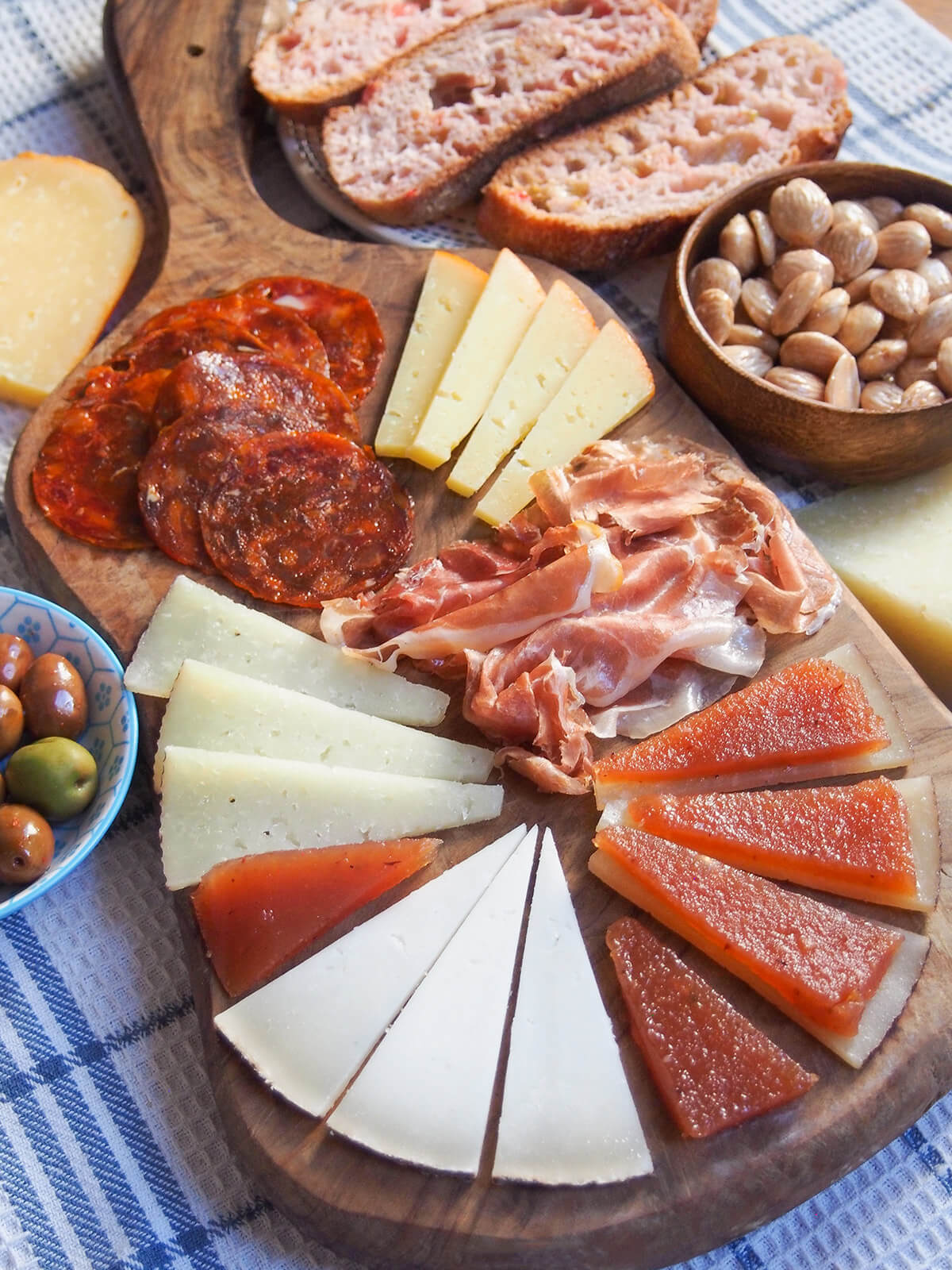 slices of Spanish cheese, ham and chorizo on board with bread and almonds behind