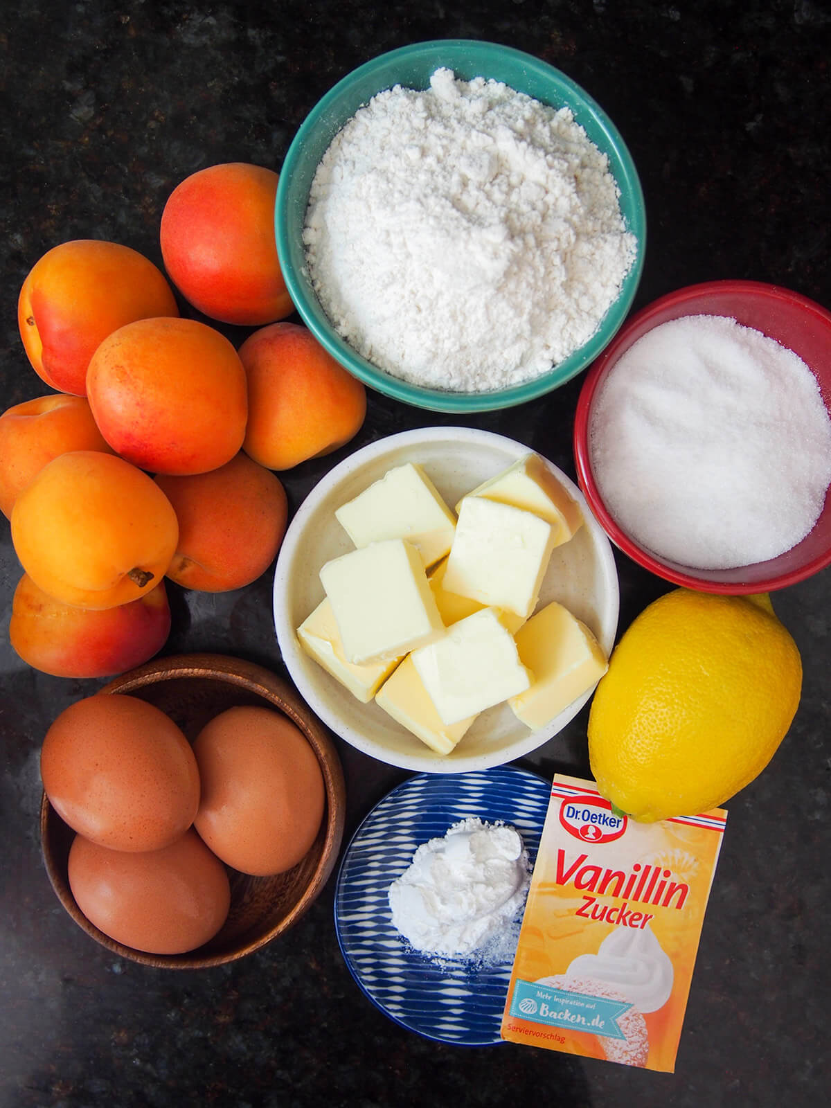 ingredients for Austrian apricot cake bowls with flour, butter, sugar, eggs with apricots and lemon to side