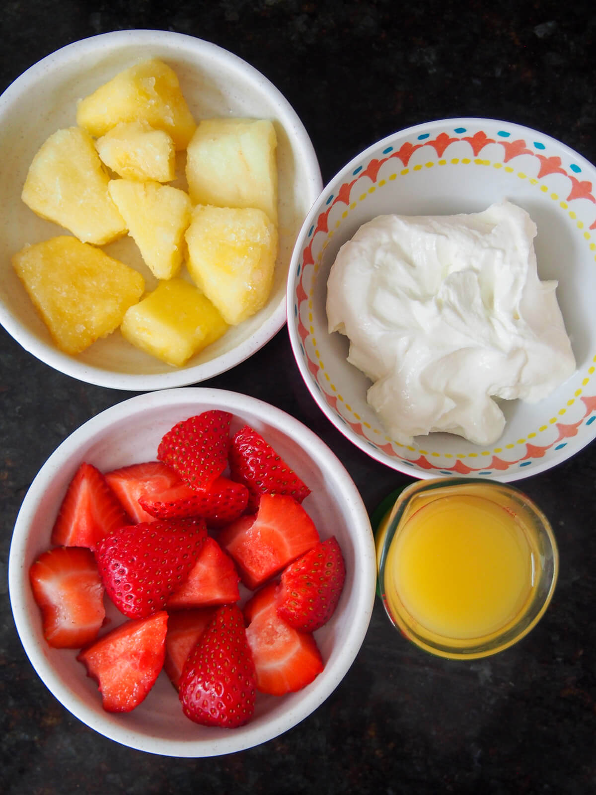 bowls with strawberry, pineapple, yogurt and glass of orange juice