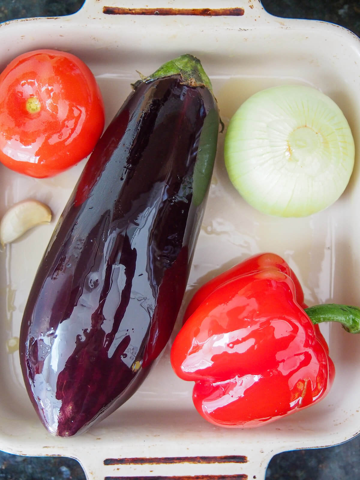 eggplant, onion, pepper, tomato and garlic in oven dish all coated with oil
