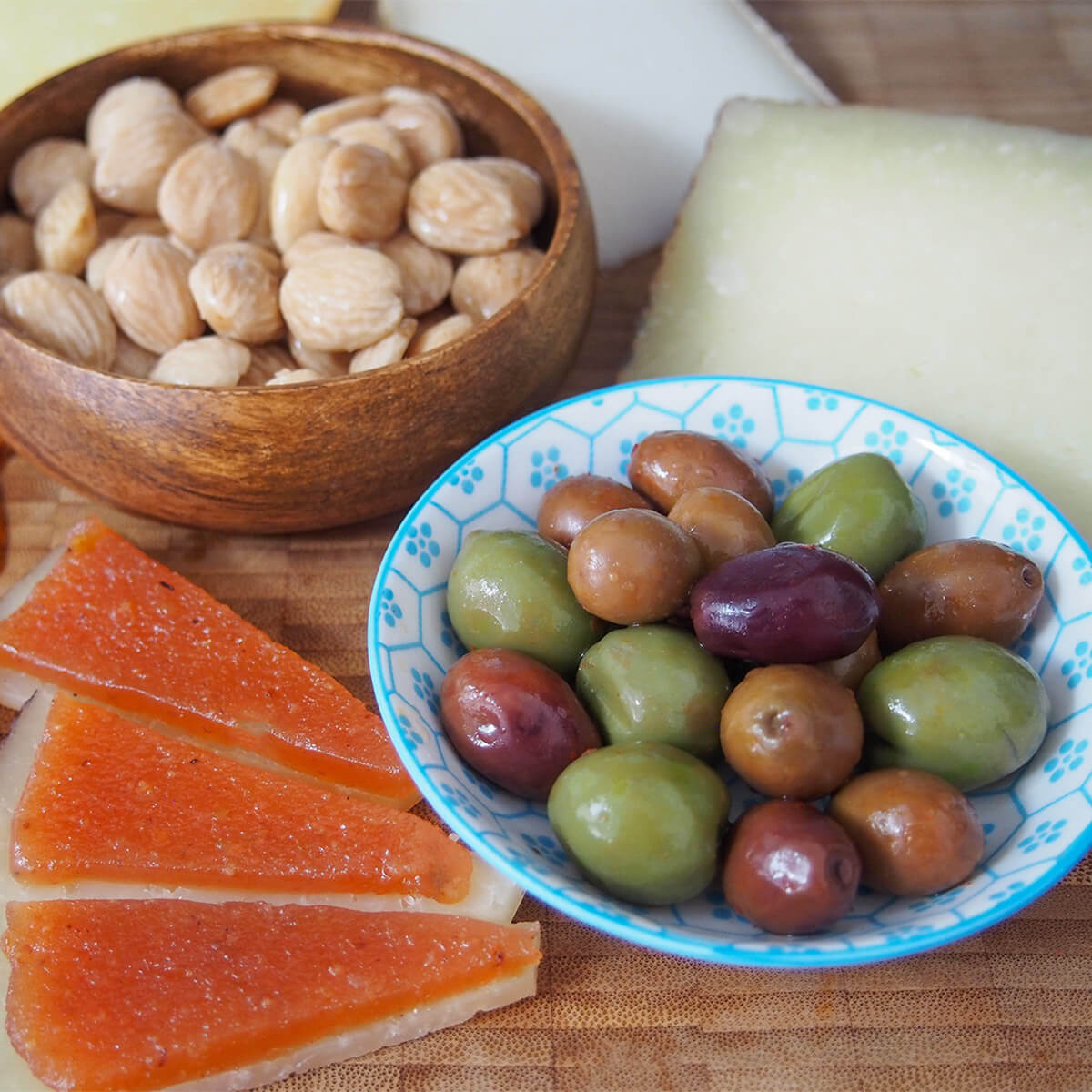 bowls with olives and almonds with quince paste on slices of cheese to side