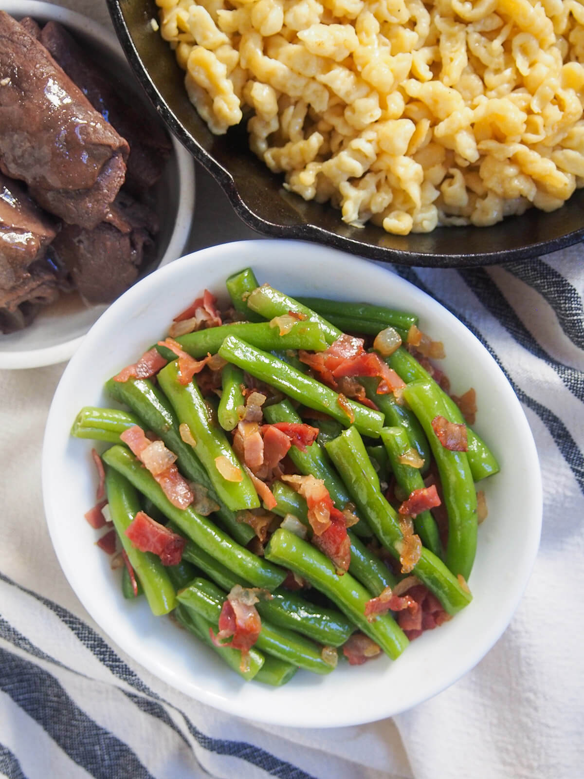 bowl of German green beans from overhead with skillet of spaetzle above