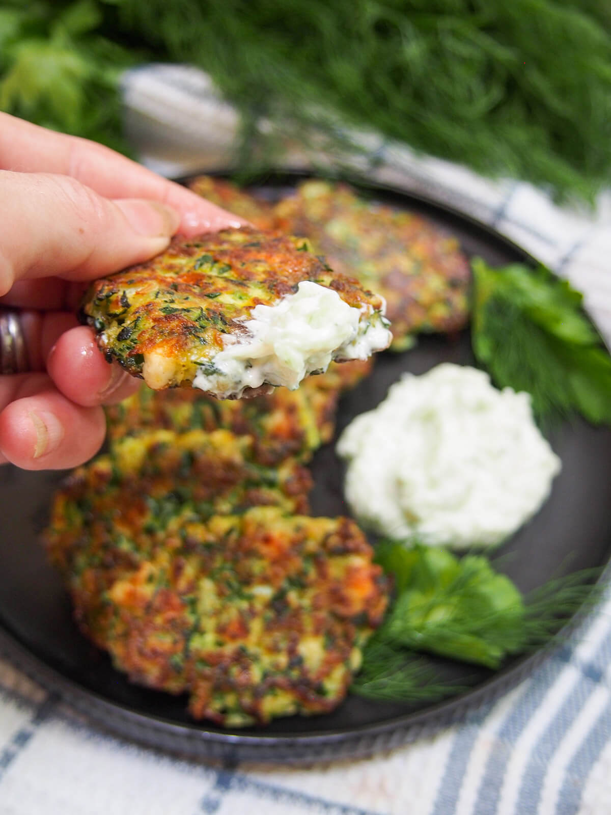 holding a zucchini fritter in hand with some tzatziki on the fritter
