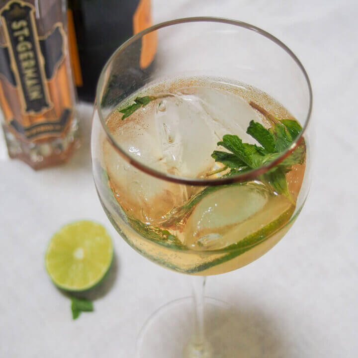 glass of Hugo spritz cocktail with cut lime to side