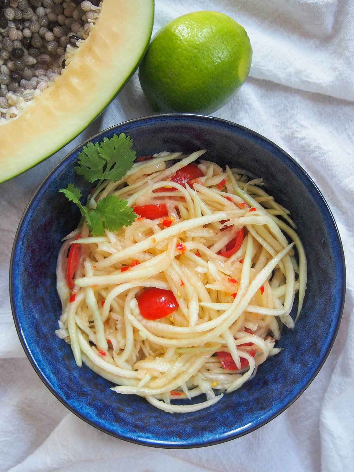bowl of Lao green papaya salad from overhead with part papaya and lime above