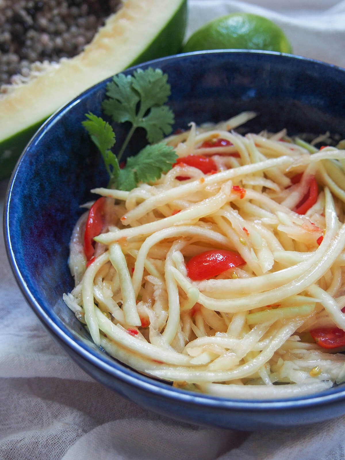 side part view of bowl of Lao green papaya salad with part papaya behind