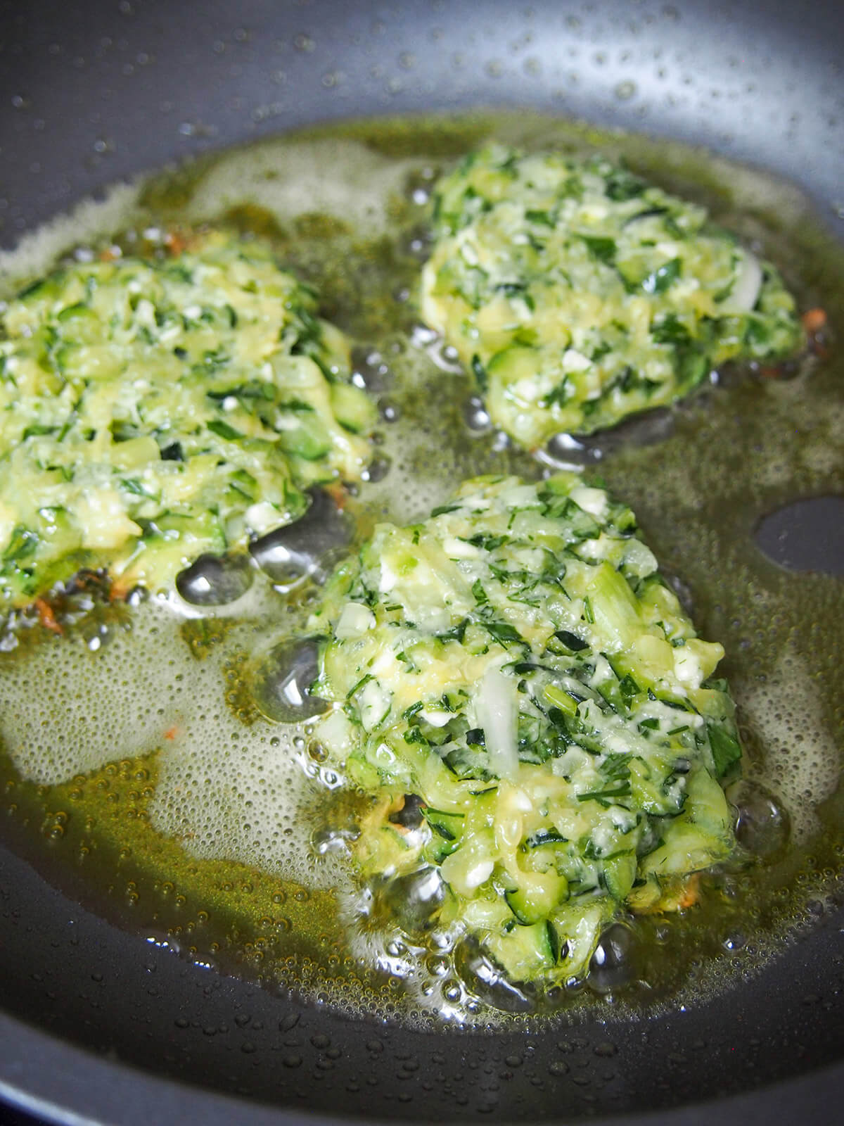 shallow frying zucchini fritters in a skillet with a thin layer of oil