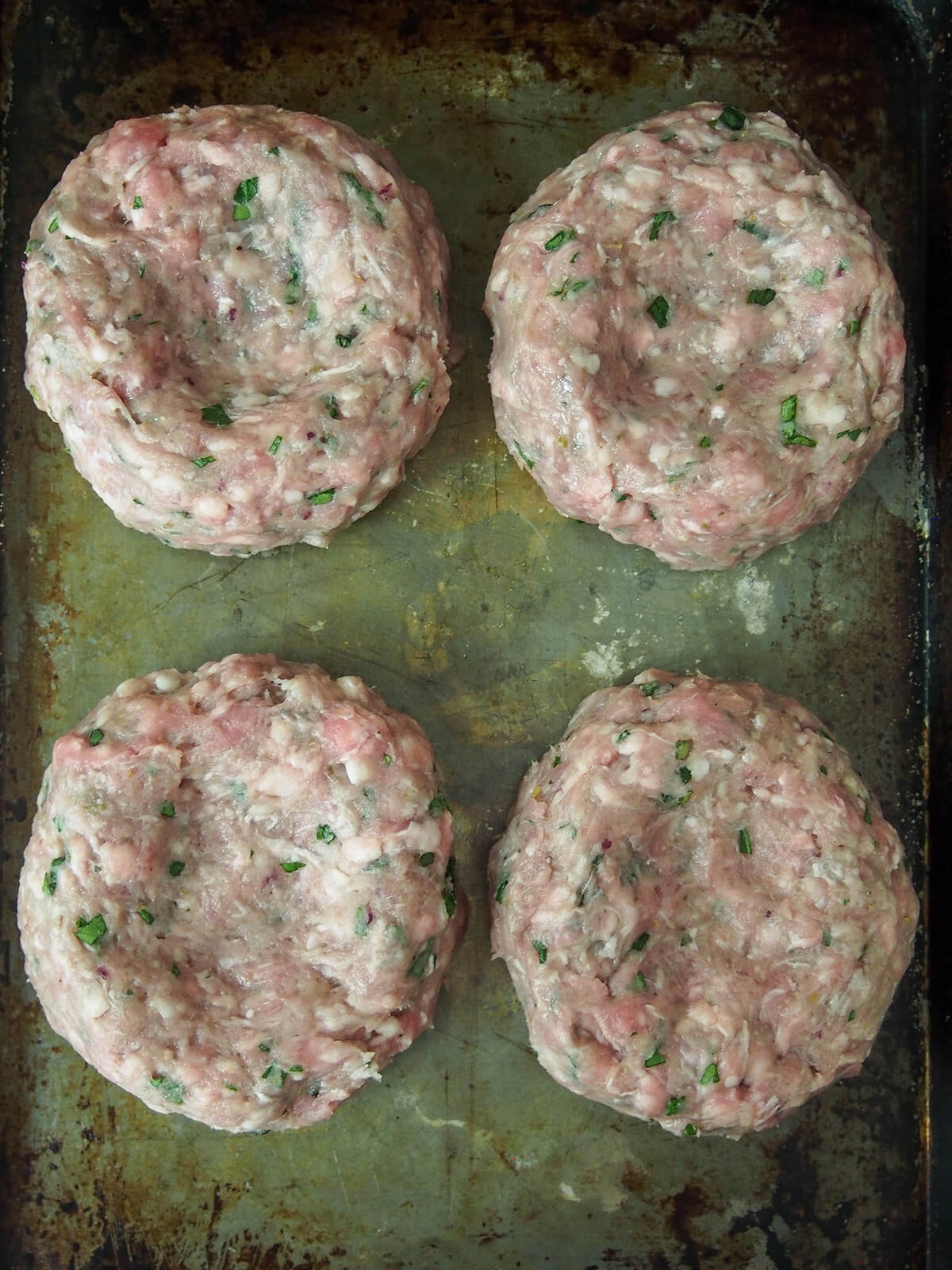 lamb burgers before cooking four lamb burgers on baking sheet with indent in each burger