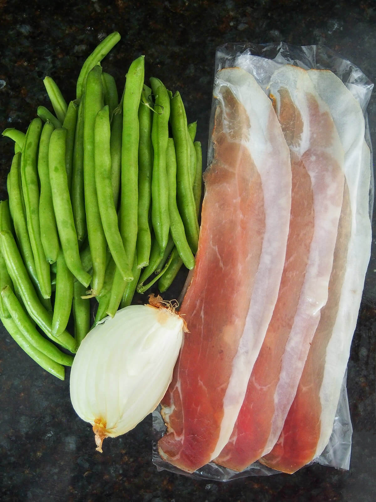 stack of green beans with slices of speck to side and chunk of onion below