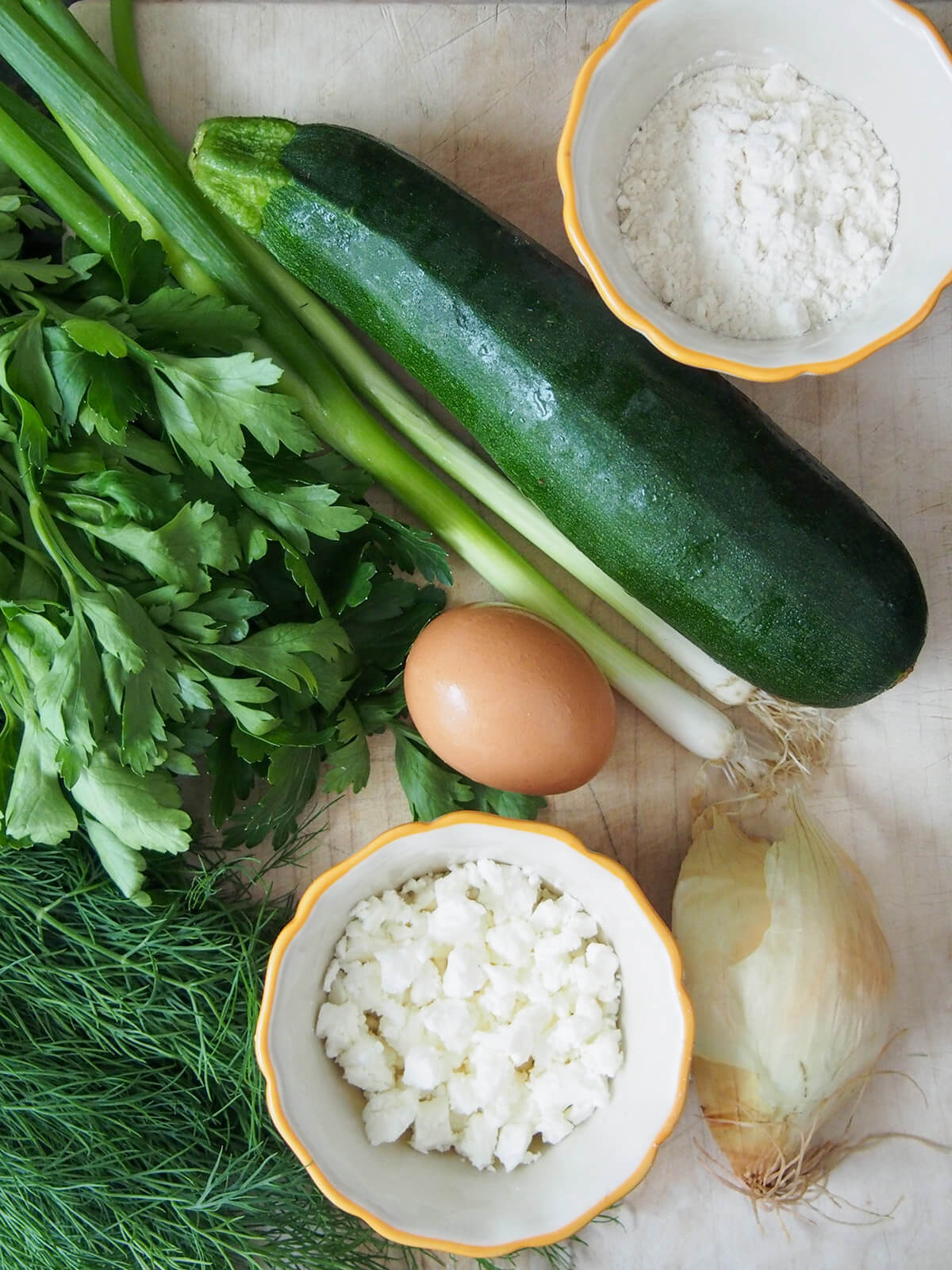 zucchini, herbs, flour, feta, onion and egg on chopping board
