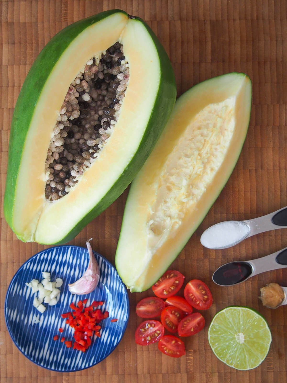 green papaya cut open with chopped cherry tomatoes, half lime and plate with chopped chili and garlic below