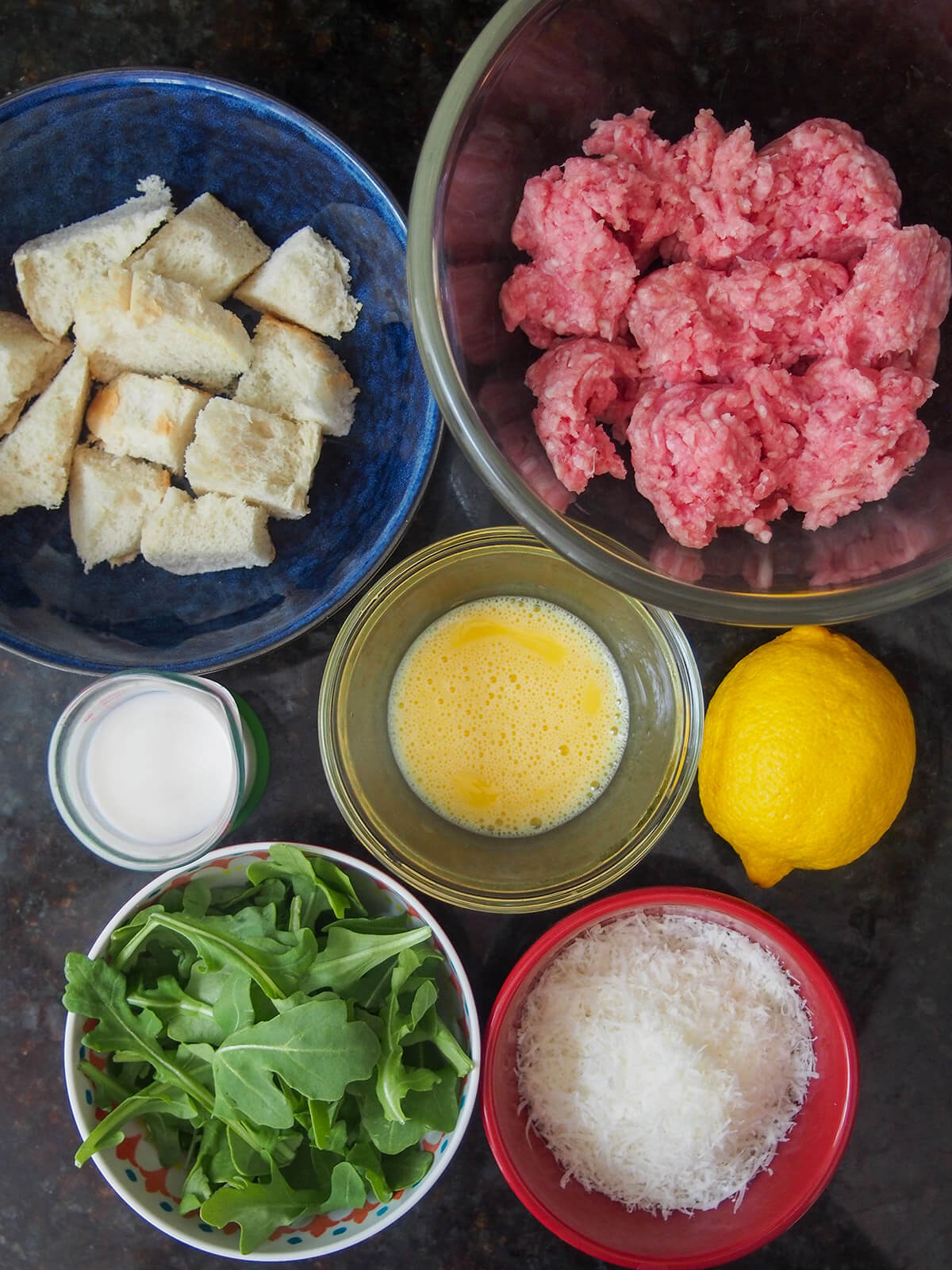bowls with ground pork, bread, egg, cheese and arugula with lemon to side