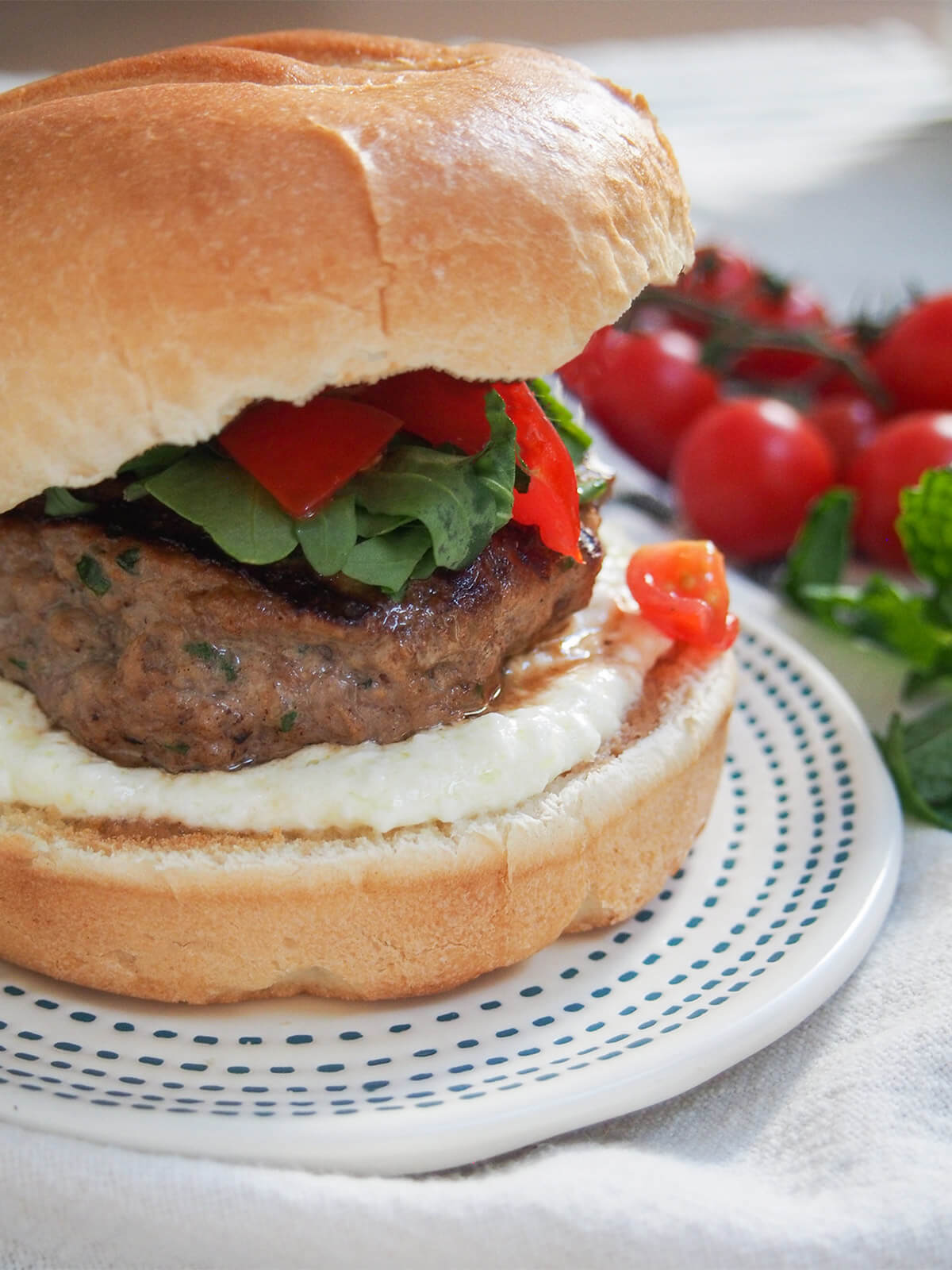 These lamb burgers are filled with Greek flavors, though they are presented in a less-than traditional way. Easy to make and incredibly tasty! side view of a lamb burger in bun