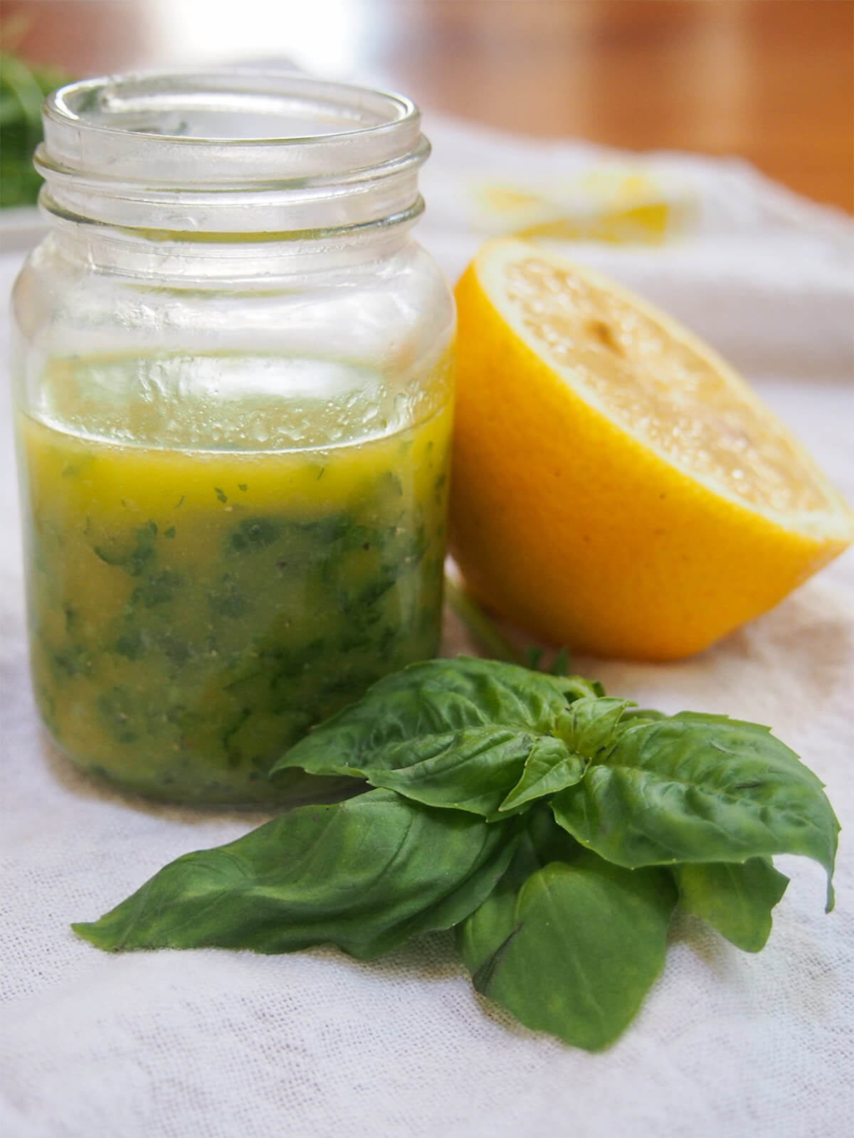 jar of lemon basil vinaigrette with lemon to side and sprig of basil in front