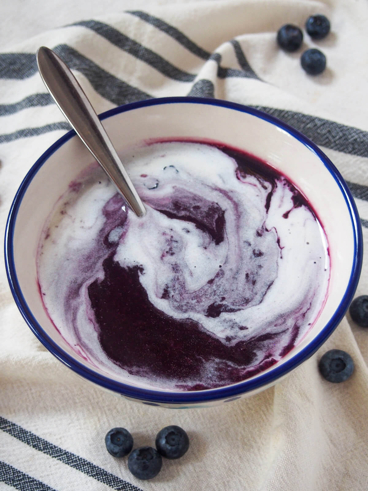 bowl of Swedish blueberry soup with spoon in it swirling cream
