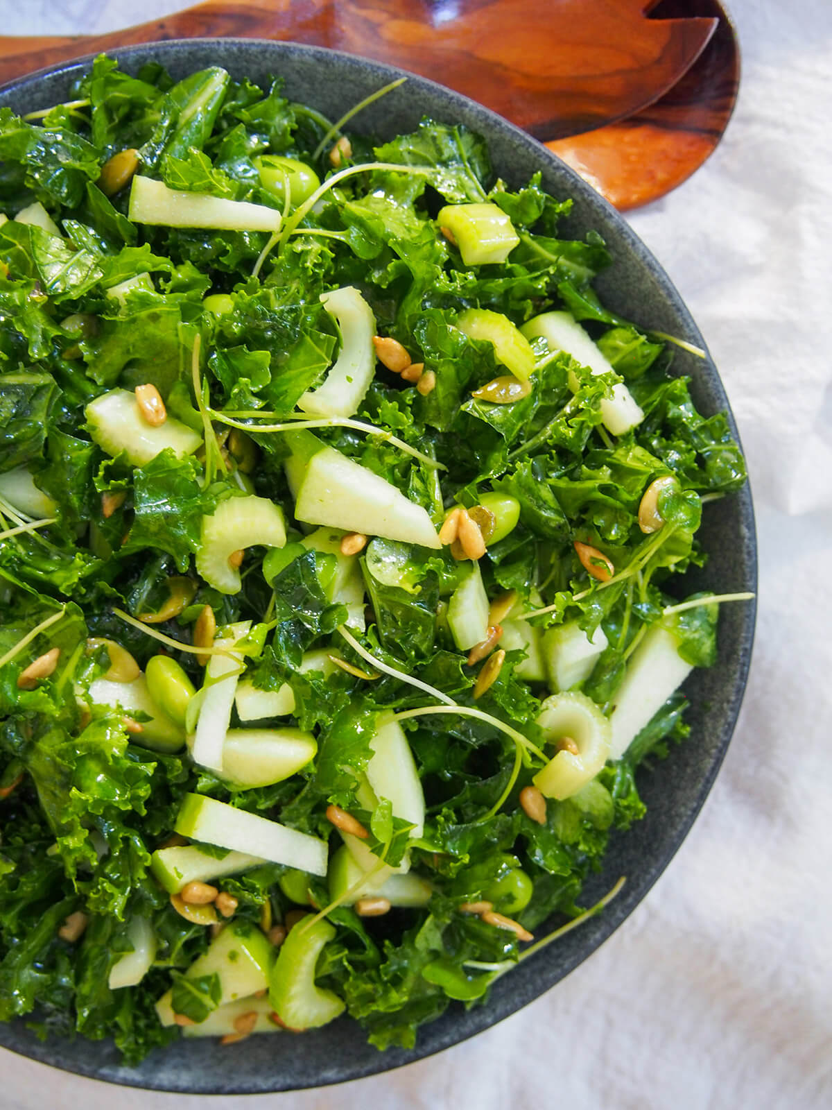 overhead view of bowl of apple kale salad with servers above bowl