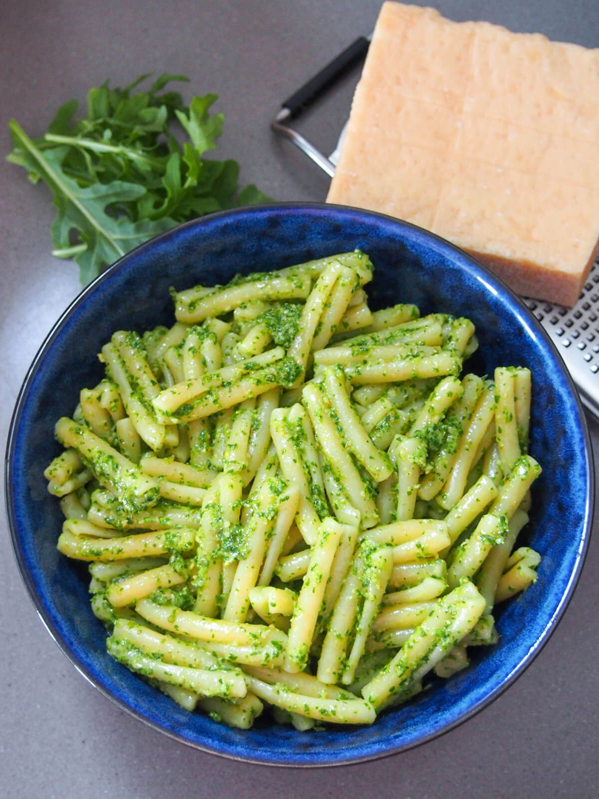 bowl of pasta with arugula pesto with block of parmesan to side