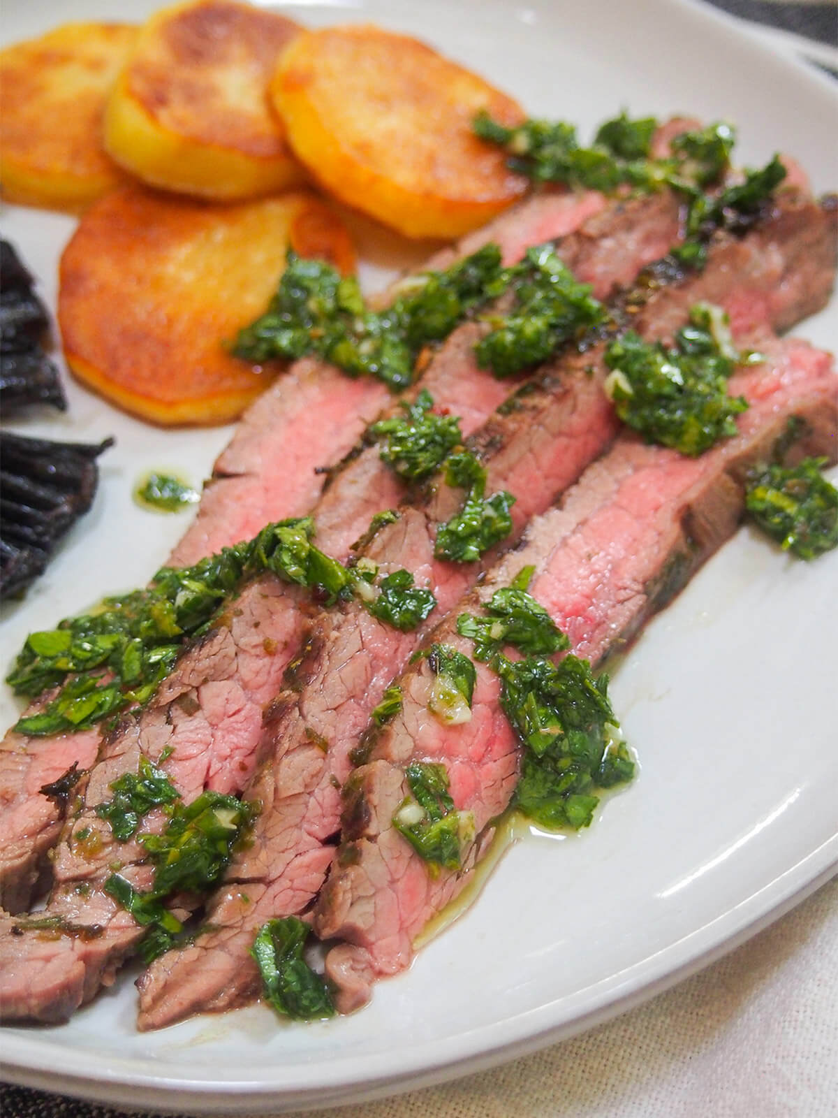 This chimichurri marinated steak is easy to make, tender and packed with delicious herb, garlic flavor. Perfect for an easy, flavorful meal, and a great way to make the most of a cheaper cut. close view of chimichurri marinated steak with additional sauce over meat