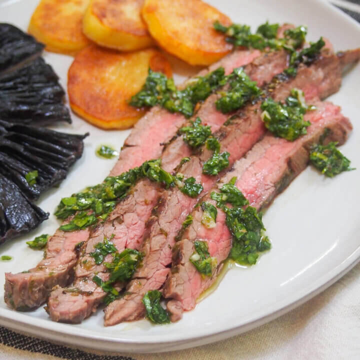 slices of chimichurri marinated steak on plae with extra sauce over meat