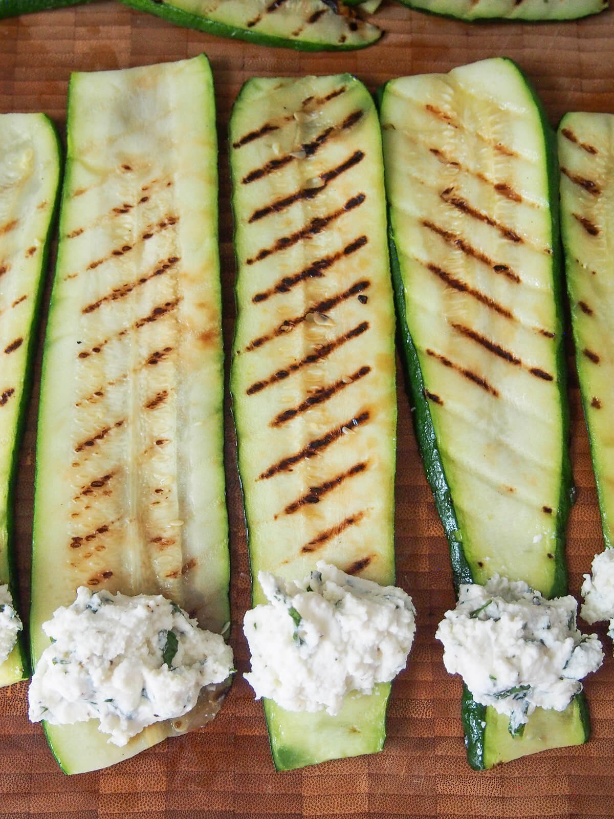 spoonfulls of ricotta herb filling at one end of slices of grilled zucchini