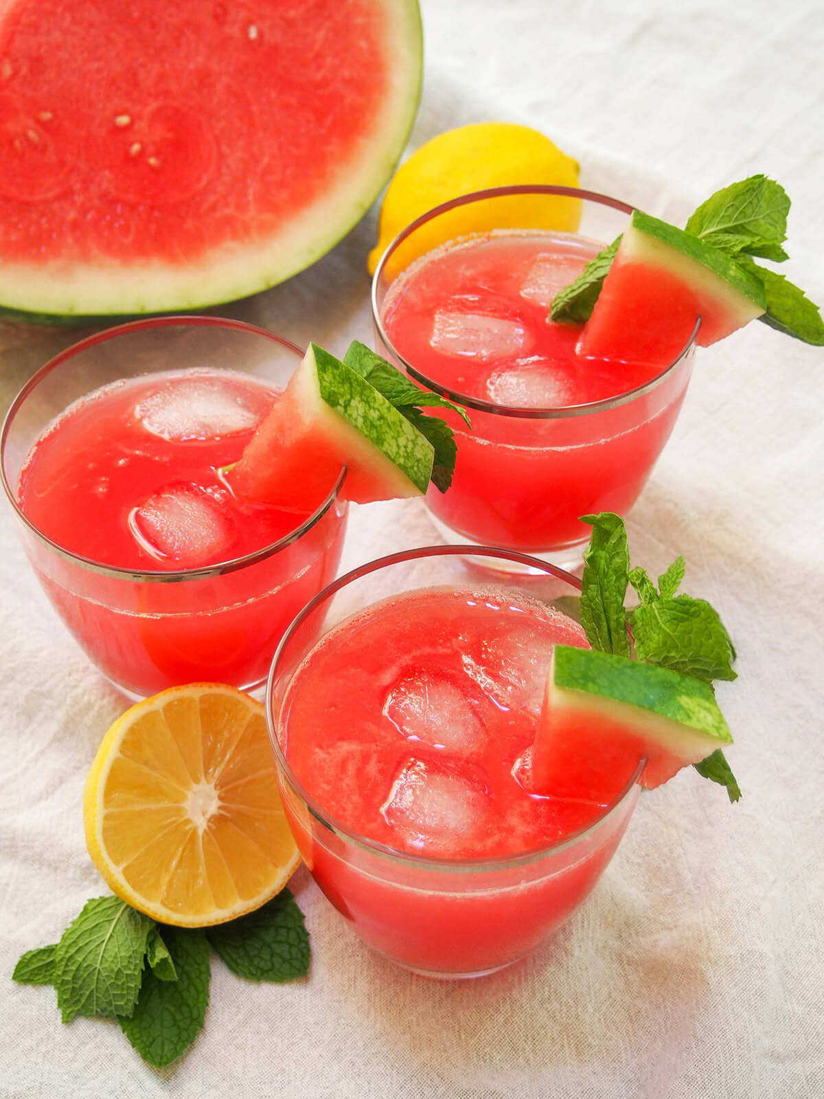glasses of watermelon mint lemonade with chunk watermelon behind