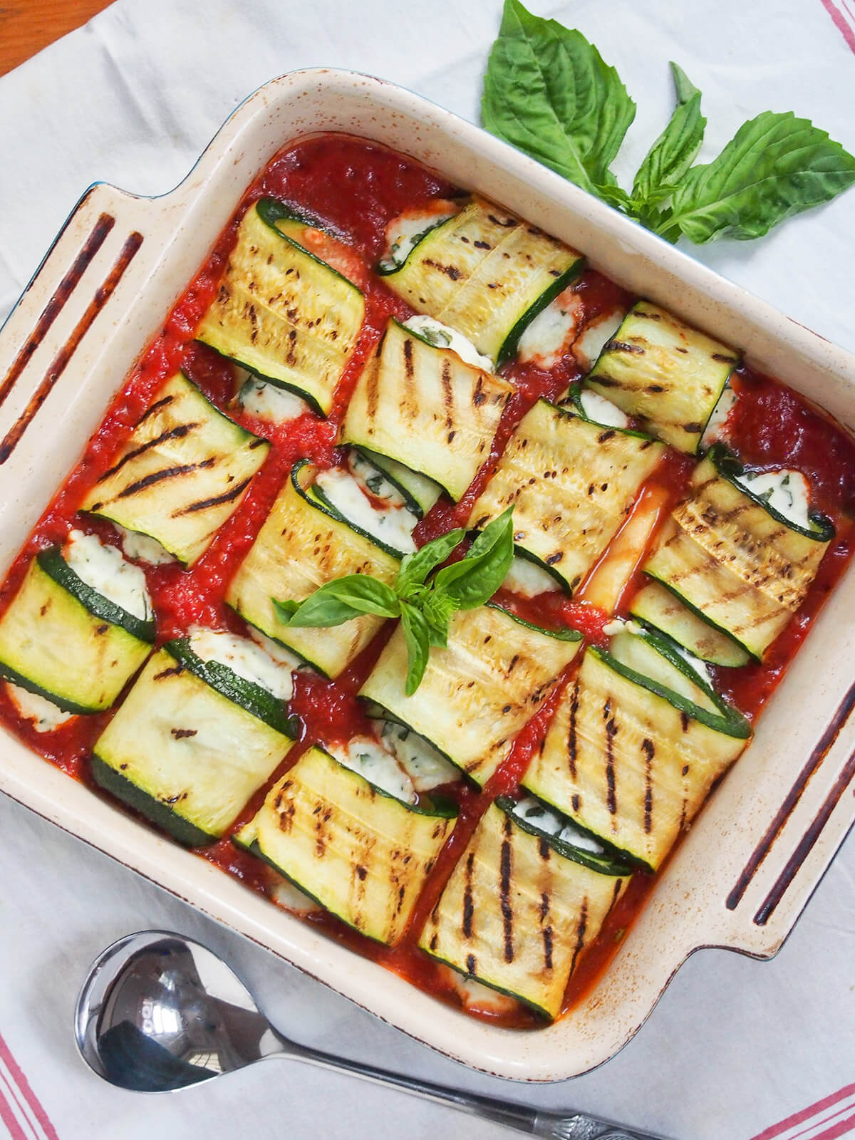 dish of zucchini involtini topped with basil and spoon below dish