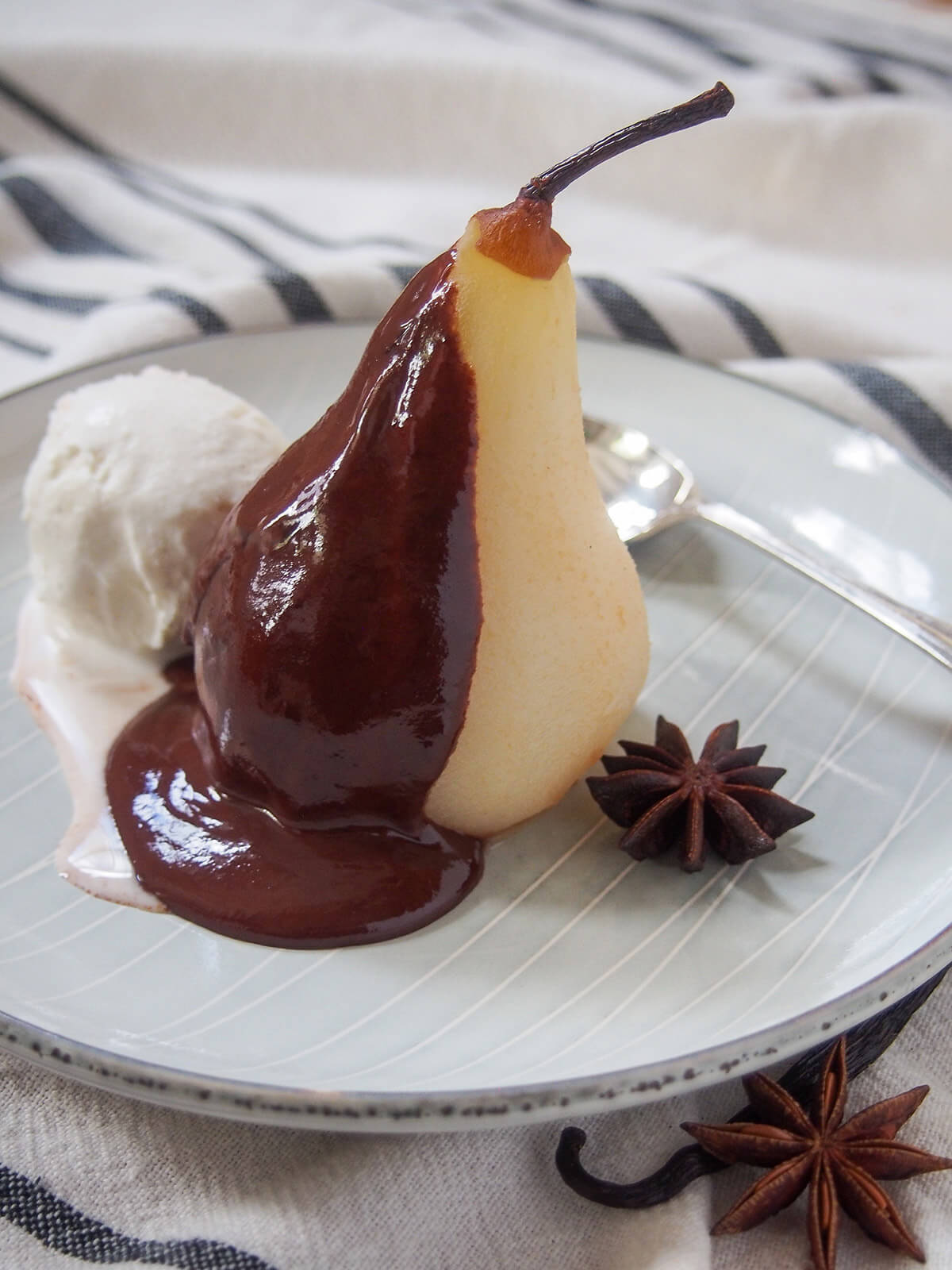 poached pear with chocolate sauce on one side and ice cream and spook behind