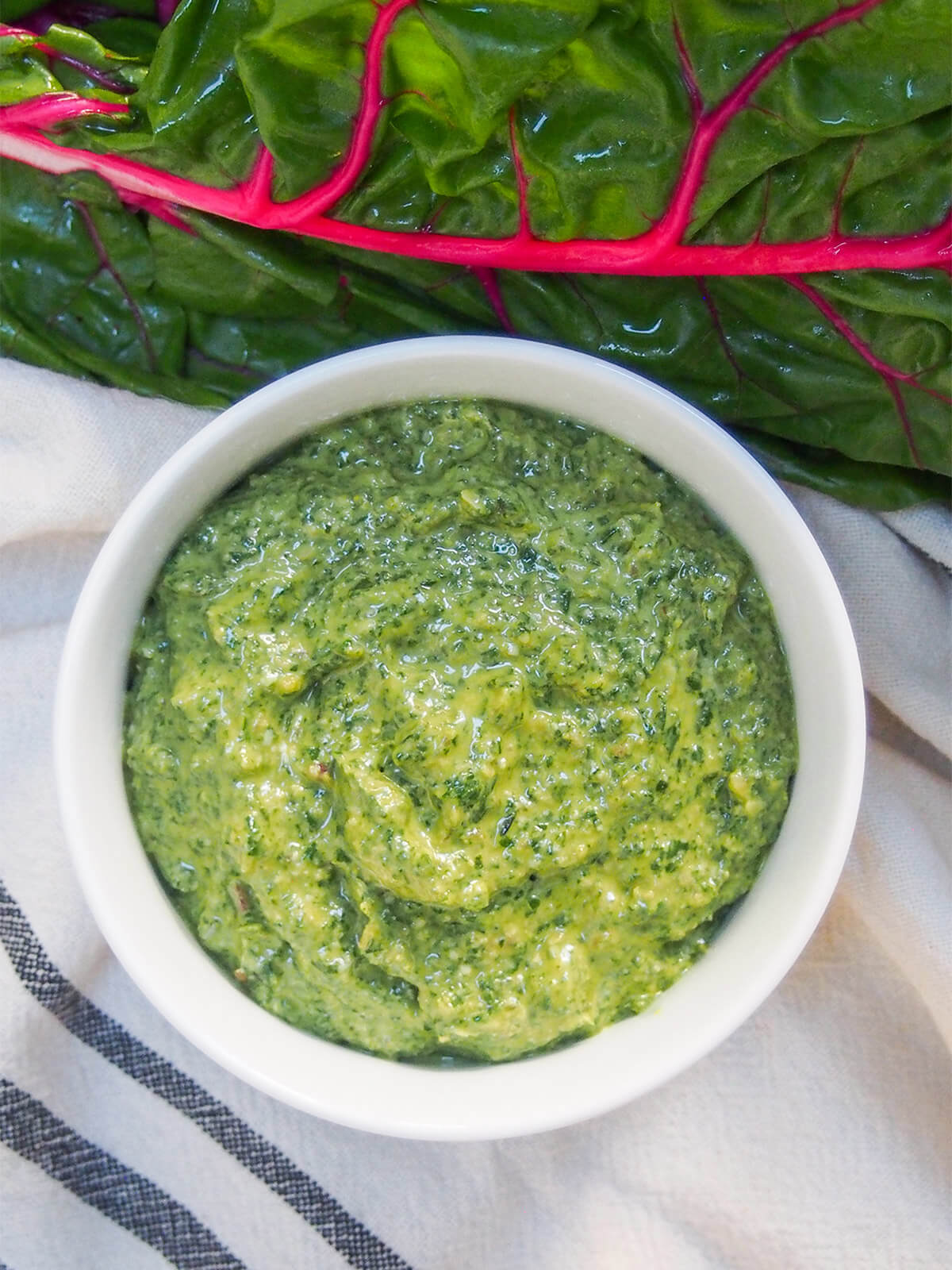 overhead view of bowl of creamy chard pesto with chard leaf above