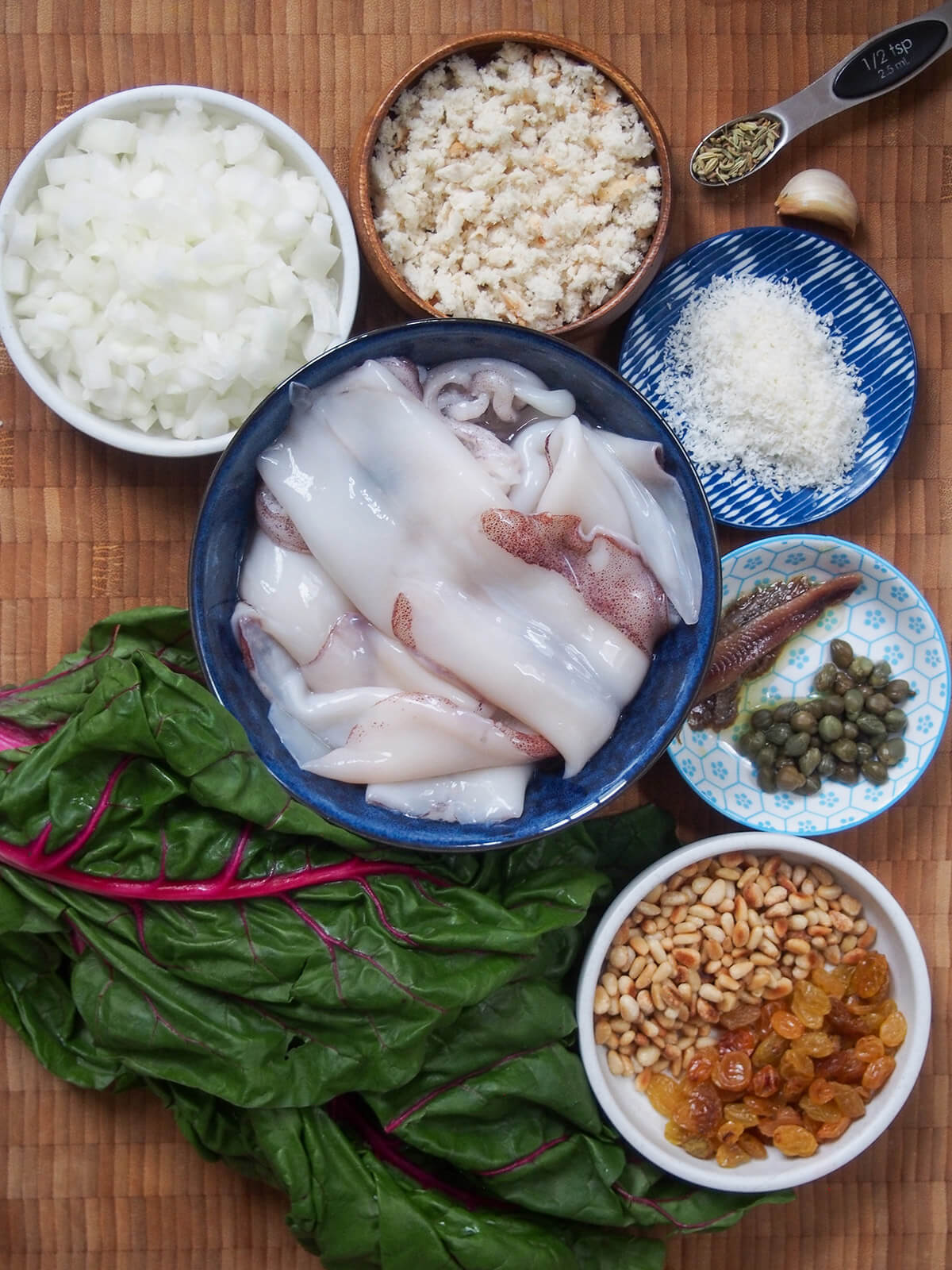 bowl of squid, onion, breadcrumbs, cheese, pine nuts, raisins, capers, anchovies and chard leaves to bottom