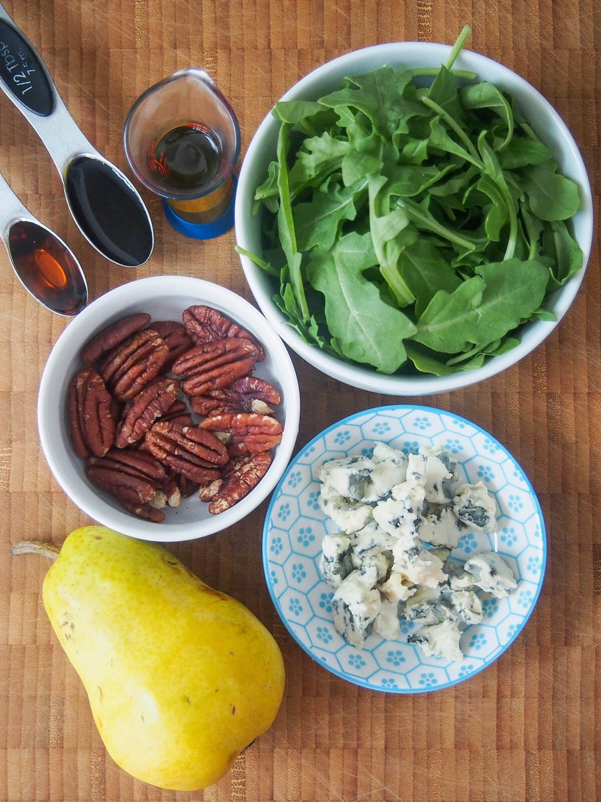 ingredients for pear gorgonzola salad bowls with arugula, pecans, gorgonzola with pear, oil, vinegar and maple to side