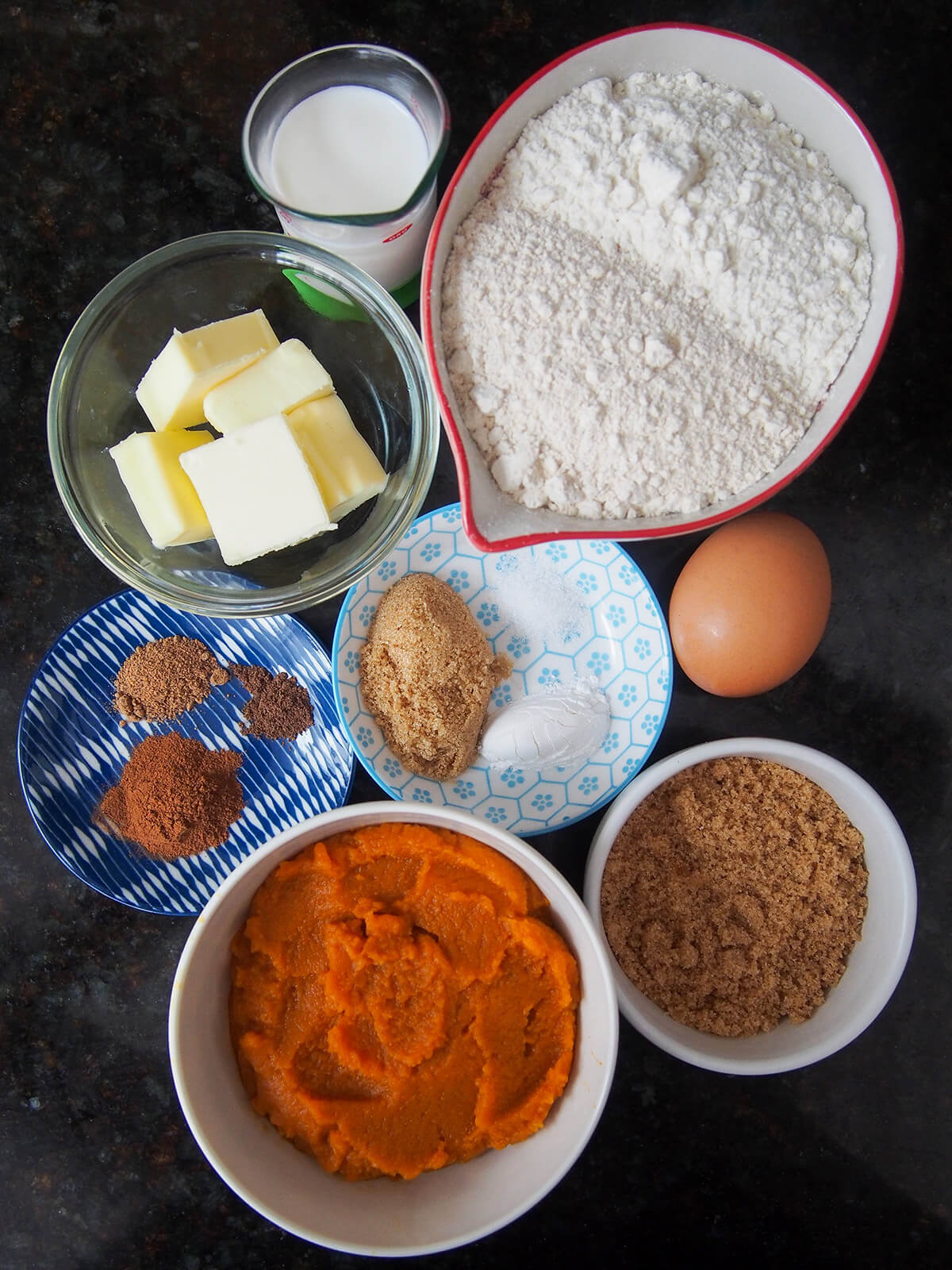 bowls with flour, sugar, butter, pumpkin puree and spices with egg and milk to side