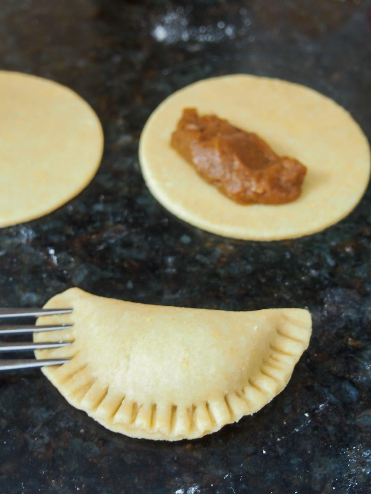 sealing an empanada with fork with some of filling on dough disc behind