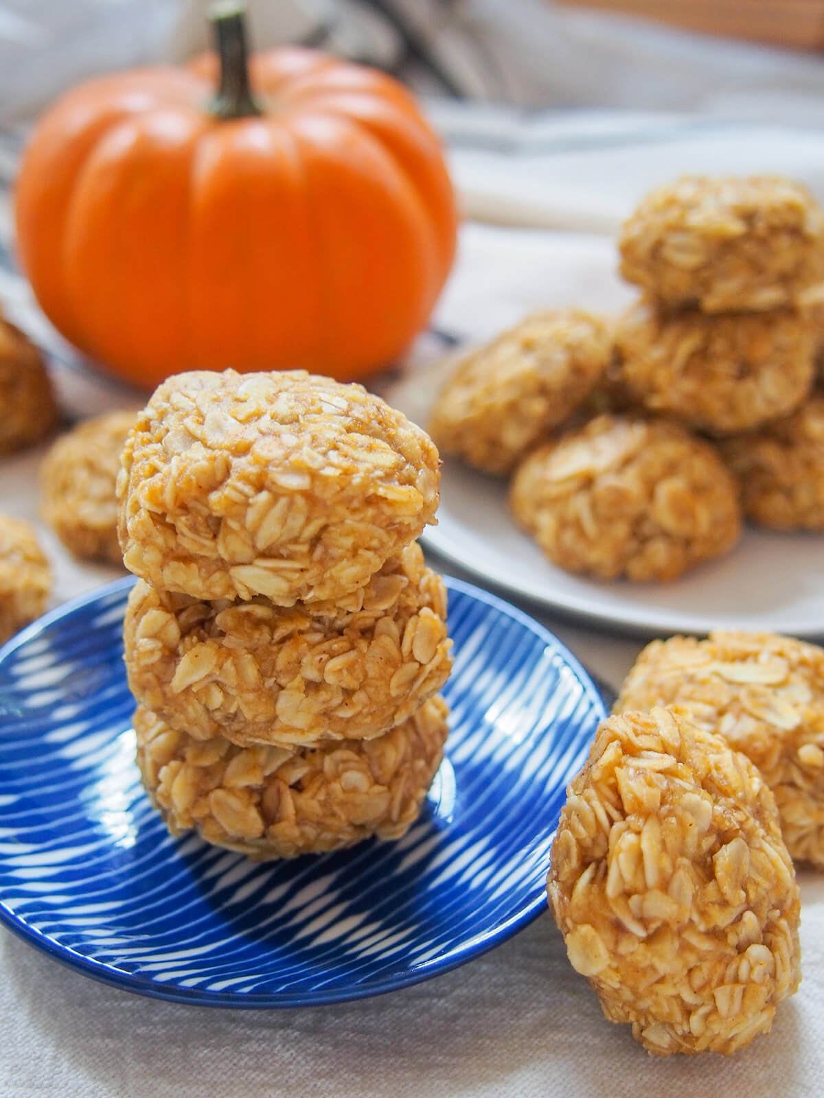 three no bake pumpkin cookies on blue plate with more cookies and small pumpkin behind