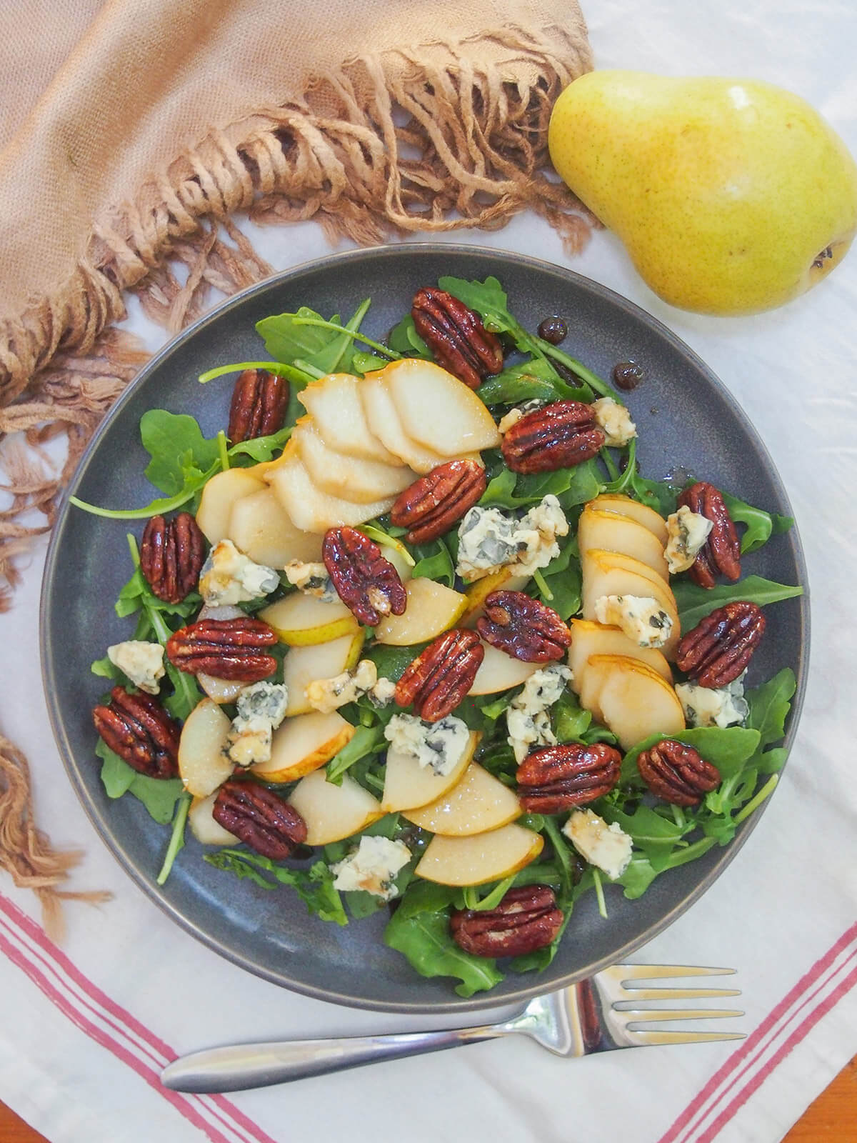 This pear gorgonzola salad is so easy to make and has a great mix of flavors. Plus don't skip the maple candied pecans that add a delicious crunch and sweetness. Great as a side, a light appetizer, or enjoy a bigger serving as a lunch. plate of pear gorgonzola salad from overhead with pear above plate and fork below