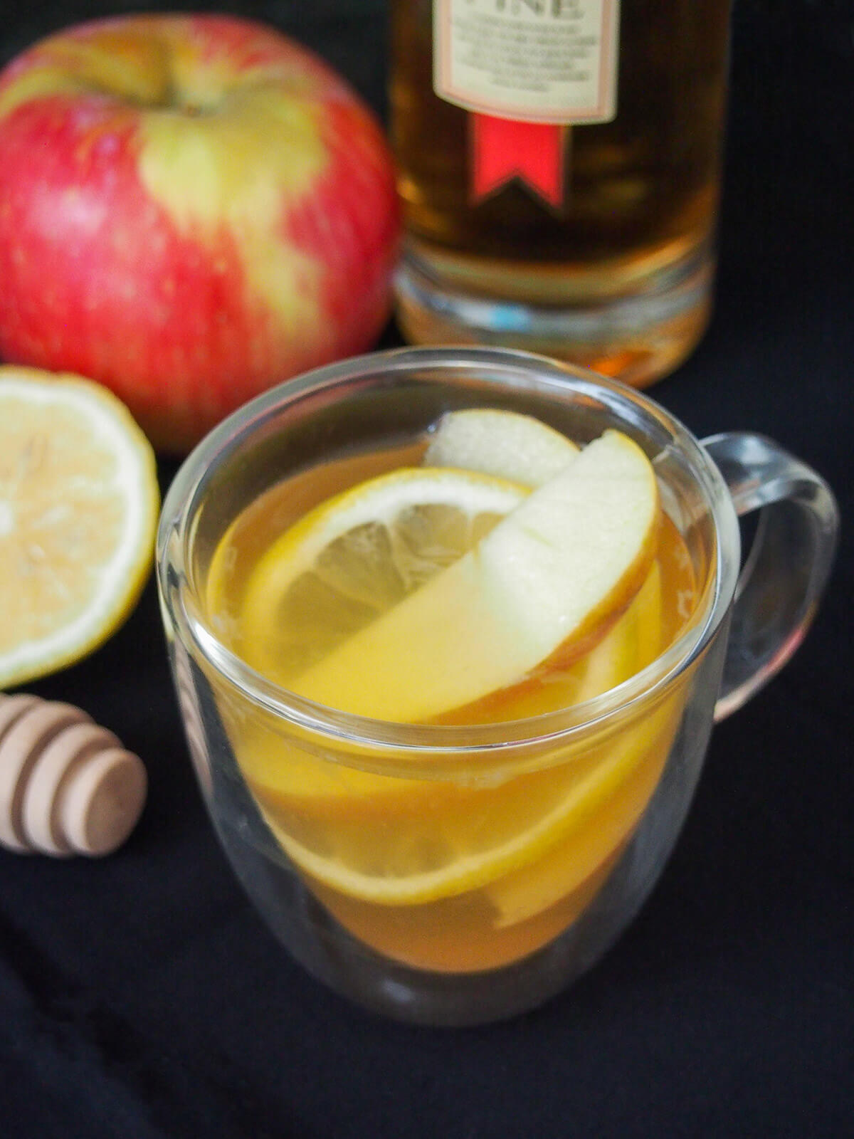 glass of apple brandy hot toddy with apple and bottle behind