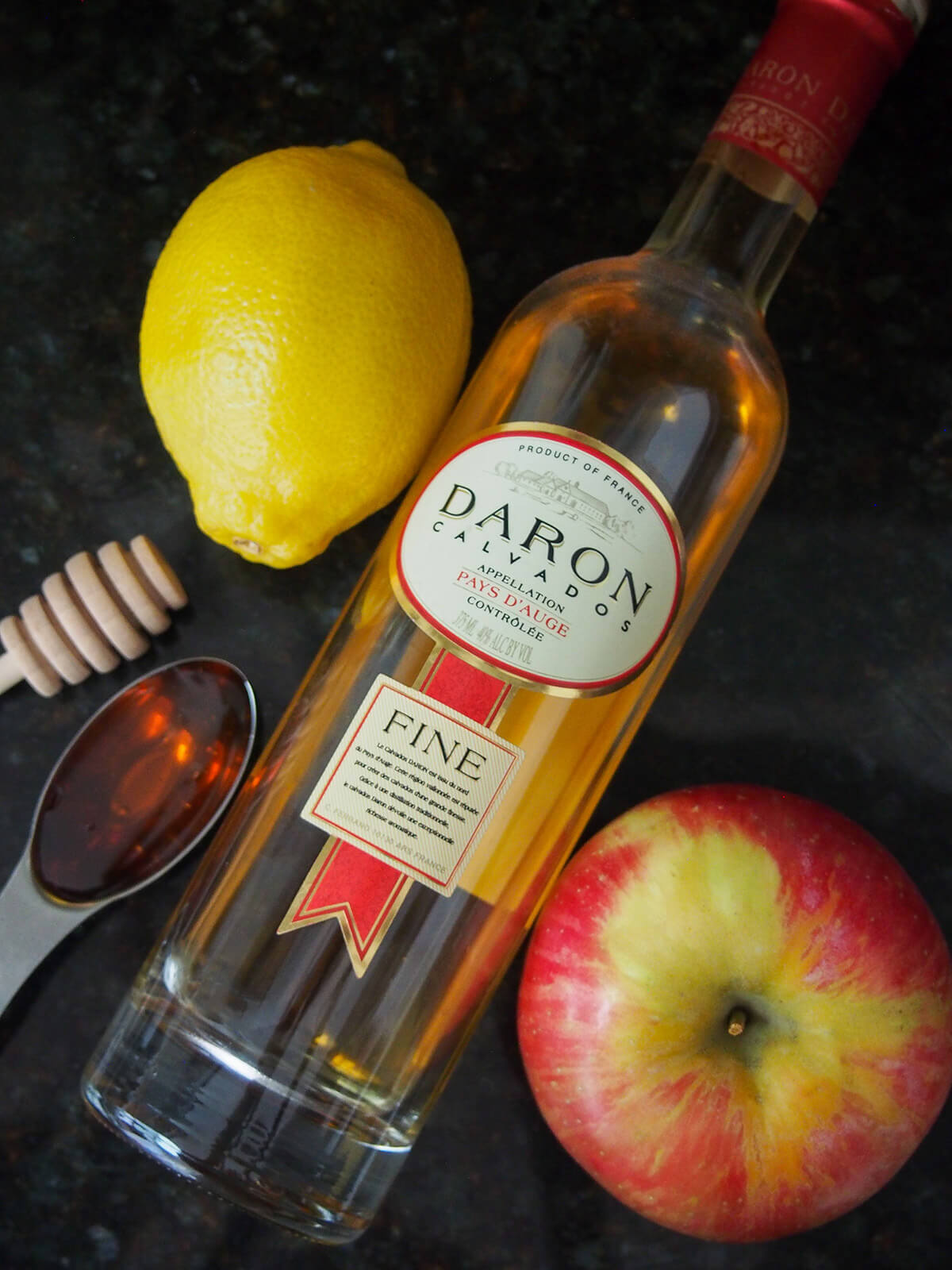 bottle of calvados with lemon and honey on one side, apple on other
