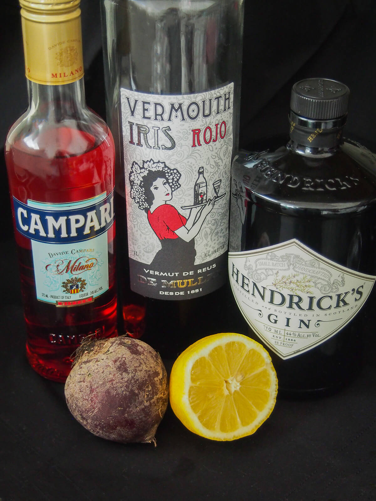 bottles of campari, vermouth and gin with beet and lemon on front
