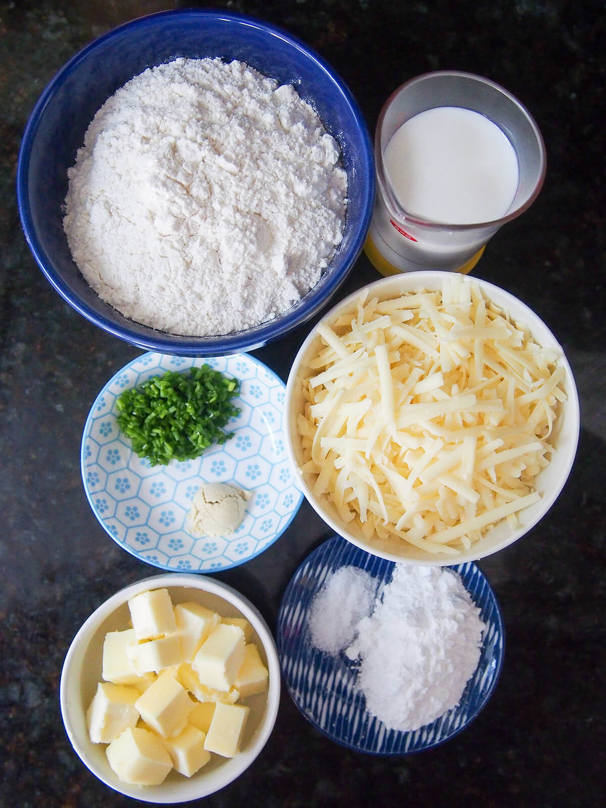 ingredients for cheese scones bowls with flout, grated cheddar, butter, raising agent, milk and chives