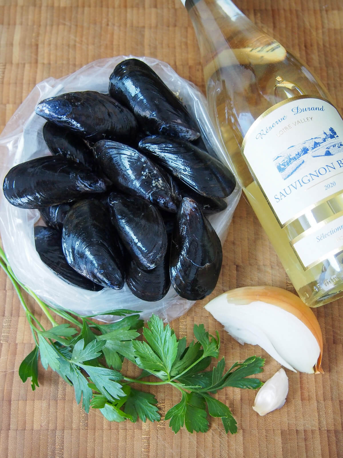 mussels, bottle of white wine, parsley, garlic and onion on chopping board