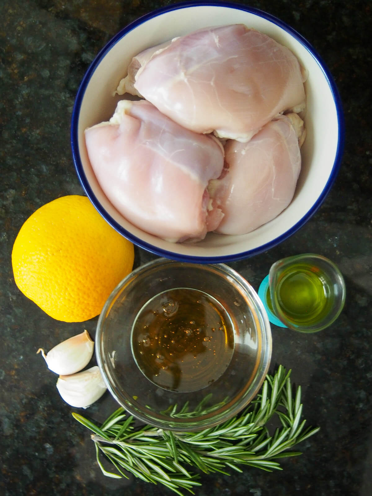 ingredients for orange rosemary chicken bowls with chicken, honey with orange to one side, rosemary, garlic and oil