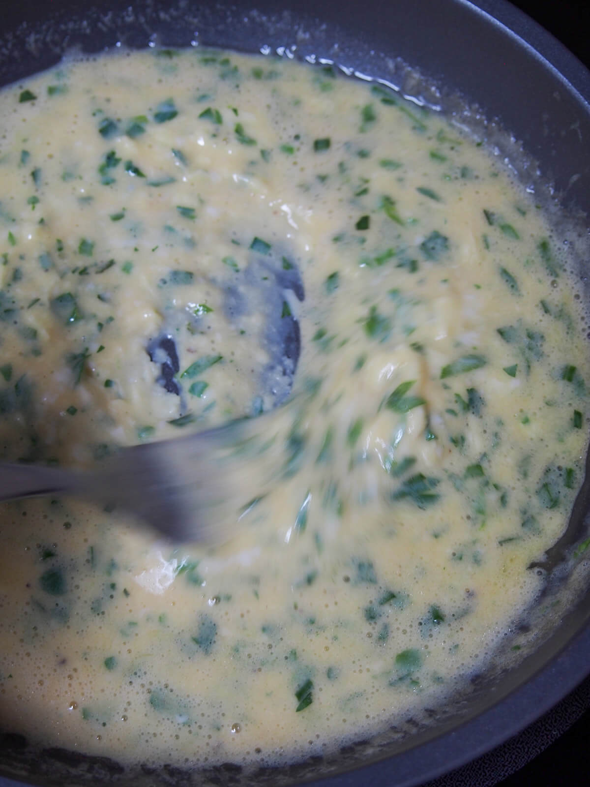 mixing egg and herb mixture in skillet as it cooks