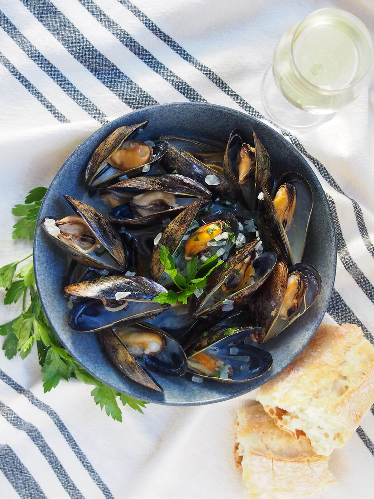 bowl of mussels in white wine with bread below bowl and glass of white wine above