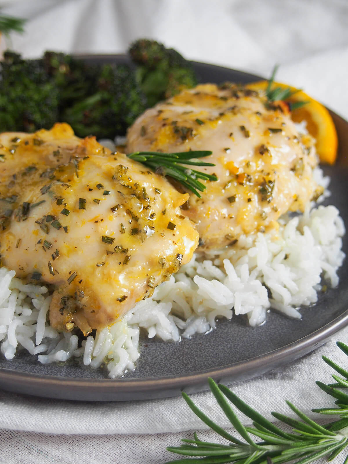 This orange rosemary chicken has a lovely combination of gently sweet and herb flavors. It's easy to prepare and perfect for any night of the week. The simple marinade comes together in no time, and then makes a tasty sauce for serving. close up view of pieces of orange rosemary chicken over rice
