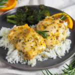 plate of orange rosemary chicken over rice with broccoli behind