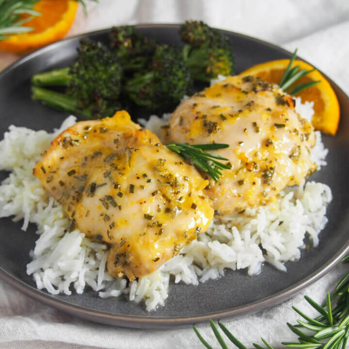 plate of orange rosemary chicken over rice with broccoli behind