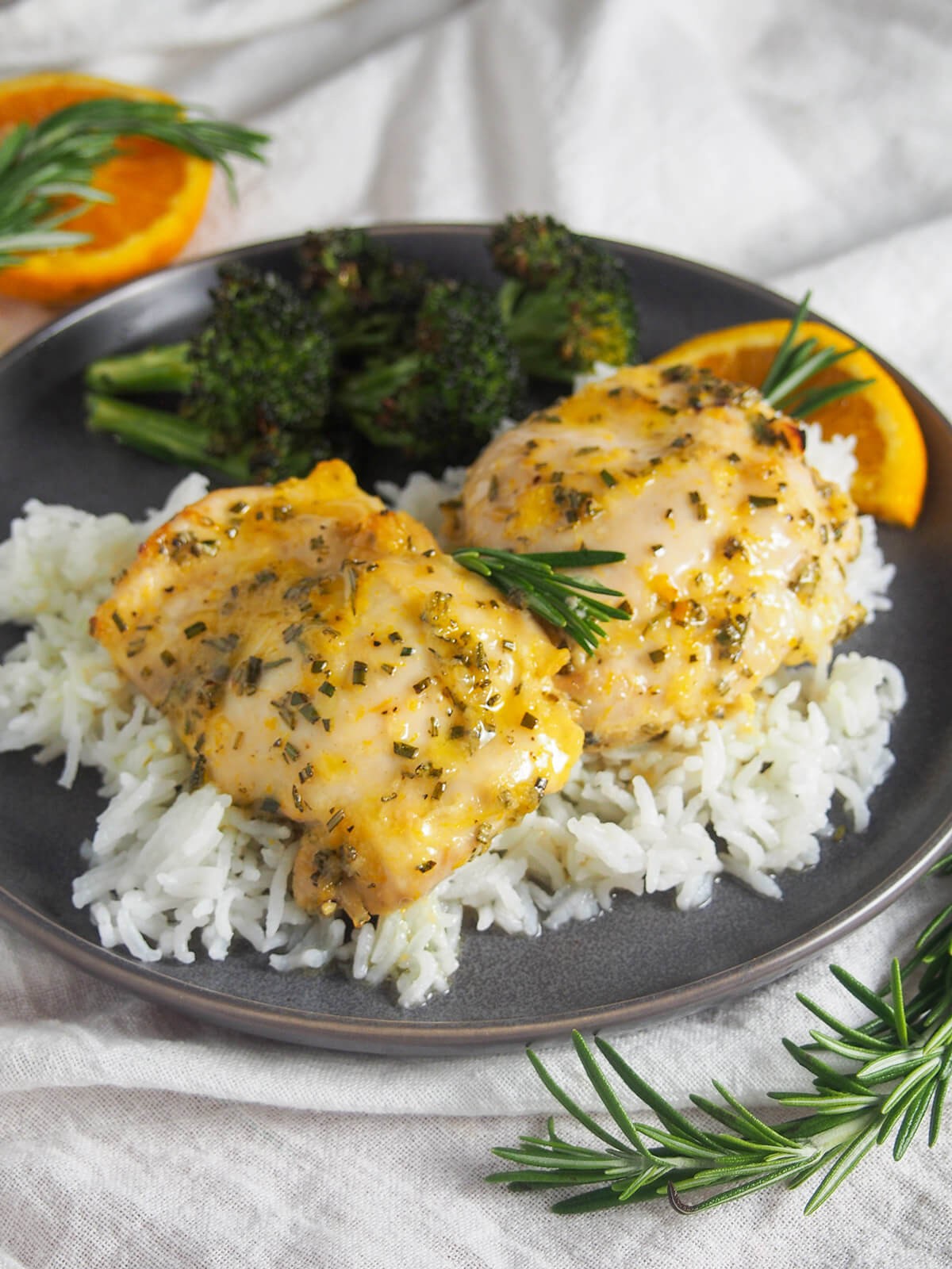 This orange rosemary chicken has a lovely combination of gently sweet and herb flavors. It's easy to prepare and perfect for any night of the week. The simple marinade comes together in no time, and then makes a tasty sauce for serving. two pieces of orange rosemary chicken over rice in plate